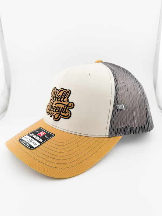 Well Sheeyit leatherette patch on birch, charcoal and amber gold trucker hat, angled view
