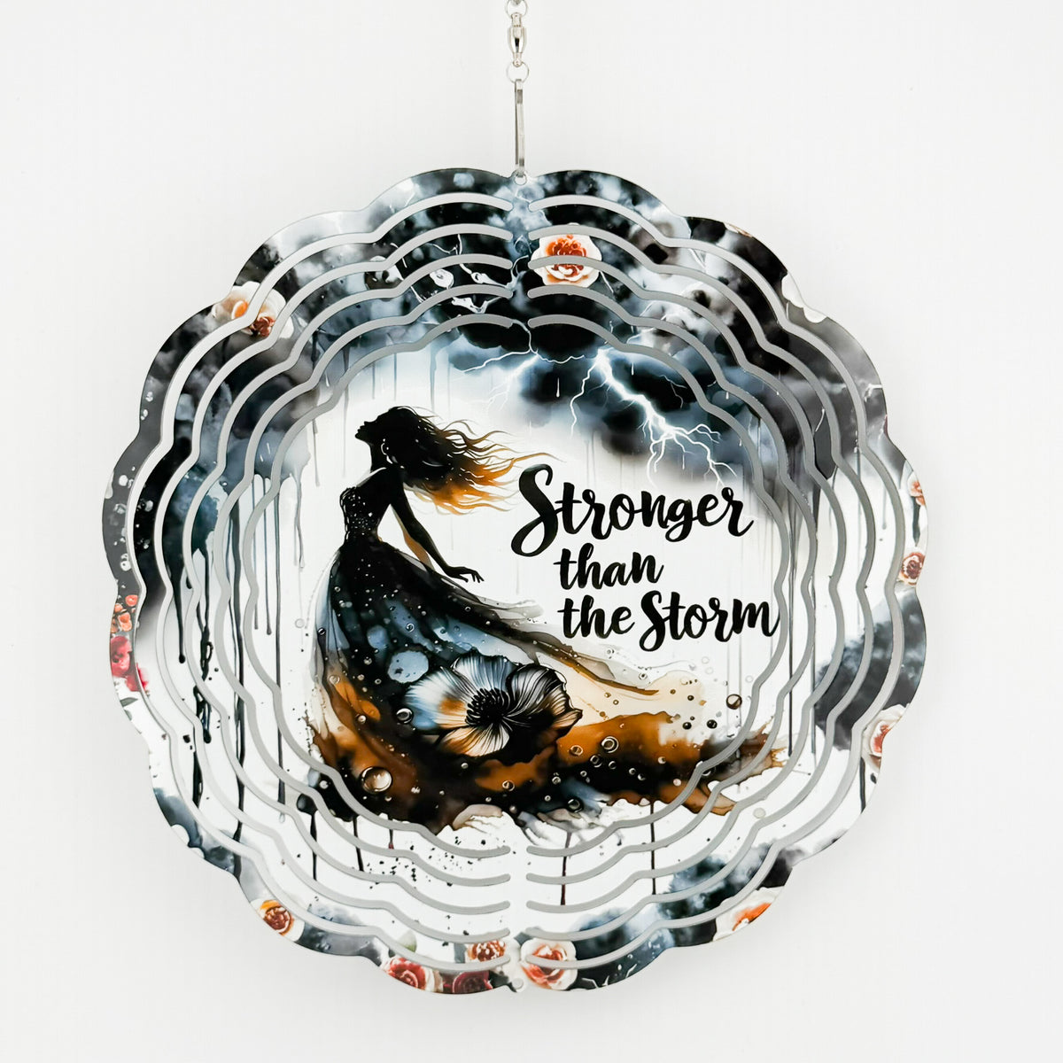 Metal wind spinner with "Stronger than the Storm" text, a woman in a flowing dress, lightning, and roses