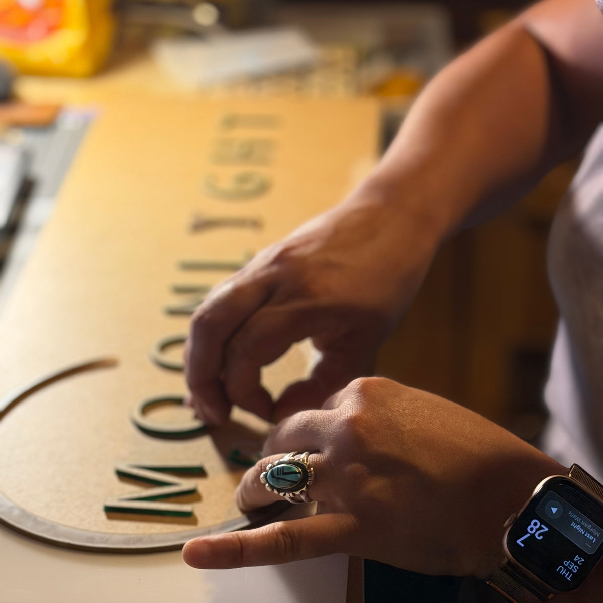 Hands placing raised green letters on a custom sign at the Hand Maid Goods workbench